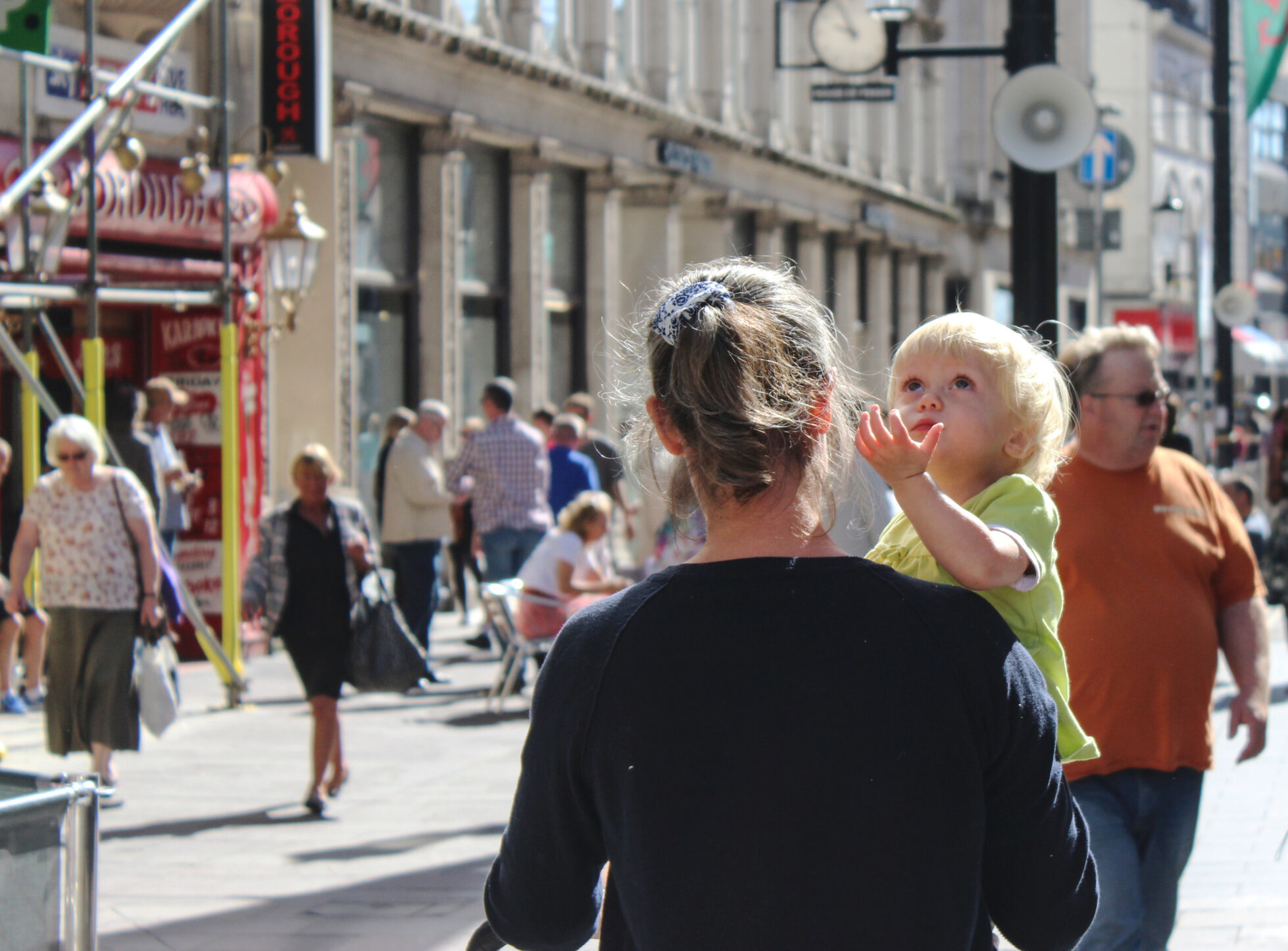 Blonde child in mother's arms is looking up to sky
