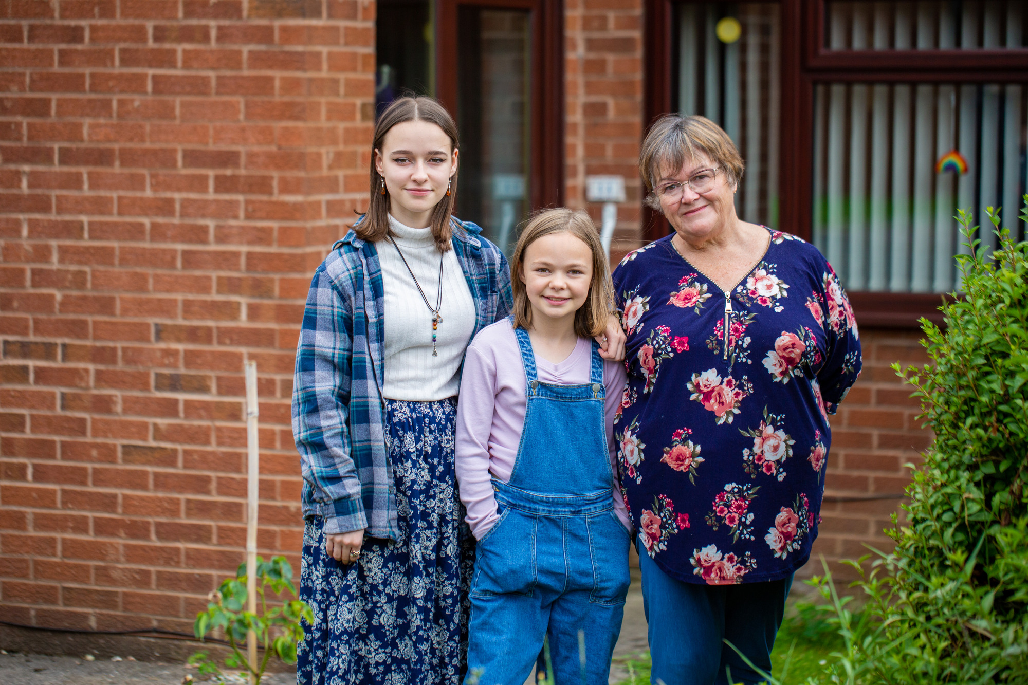 A woman a young girl and a teenage girl standing in front of the house